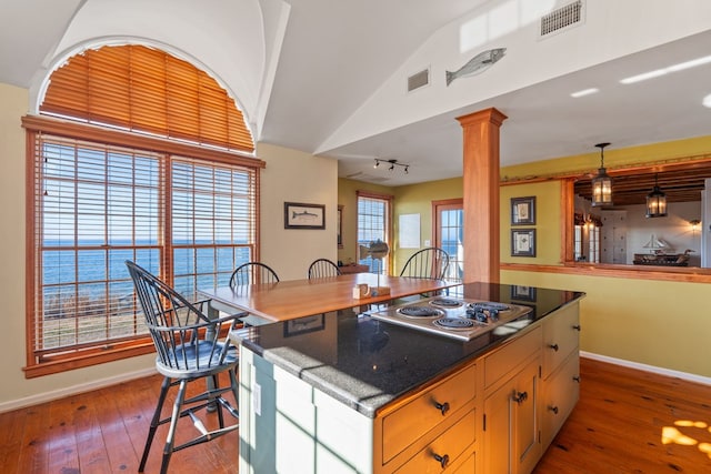 kitchen featuring pendant lighting, stainless steel gas stovetop, a water view, hardwood / wood-style flooring, and decorative columns