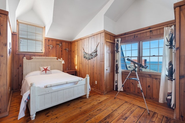 bedroom featuring wooden walls, hardwood / wood-style floors, a water view, and vaulted ceiling