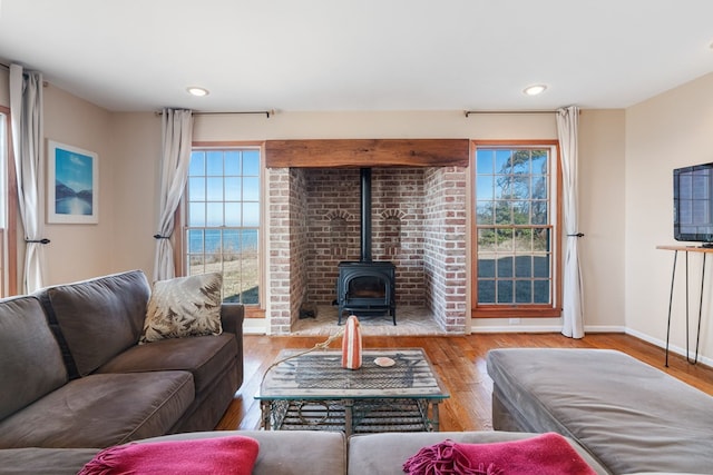 living room with a healthy amount of sunlight, a water view, a wood stove, and light hardwood / wood-style flooring