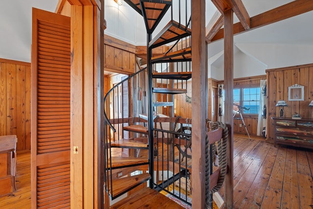 staircase featuring hardwood / wood-style floors, vaulted ceiling with beams, and wooden walls