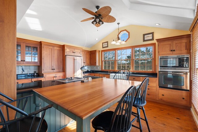 kitchen featuring backsplash, ceiling fan with notable chandelier, hanging light fixtures, built in appliances, and light wood-type flooring