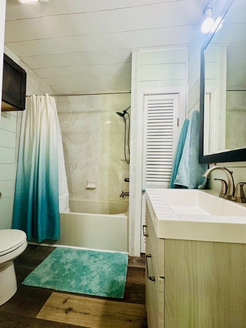 full bathroom with wood finished floors, vanity, shower / bathtub combination with curtain, and toilet