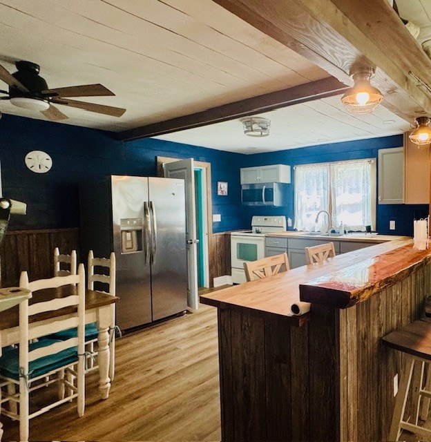 kitchen with a peninsula, beam ceiling, light wood-style floors, wooden ceiling, and appliances with stainless steel finishes