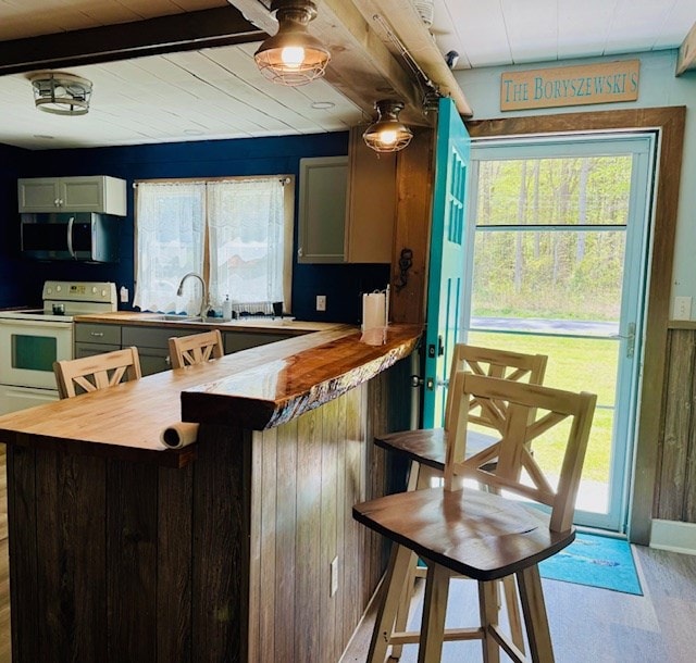kitchen with a sink, beamed ceiling, light wood finished floors, electric range, and stainless steel microwave