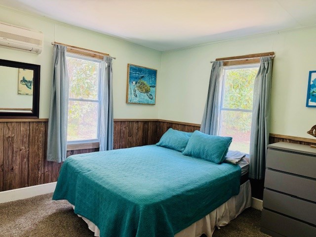 bedroom with wainscoting, dark colored carpet, an AC wall unit, and multiple windows