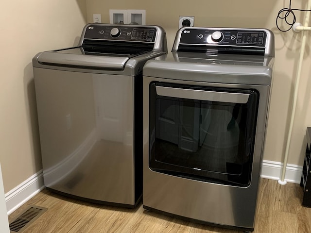 clothes washing area featuring separate washer and dryer and light hardwood / wood-style flooring