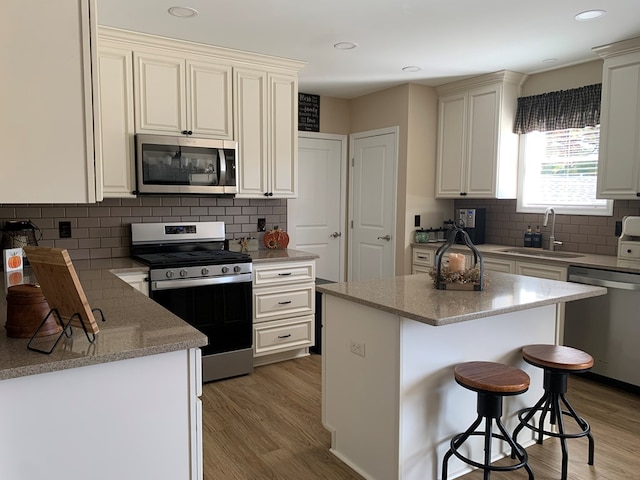 kitchen featuring sink, appliances with stainless steel finishes, tasteful backsplash, a kitchen island, and wood-type flooring