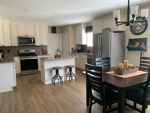 kitchen featuring appliances with stainless steel finishes, light wood-type flooring, tasteful backsplash, sink, and a center island