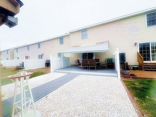 rear view of house with outdoor dining area, fence, and a deck