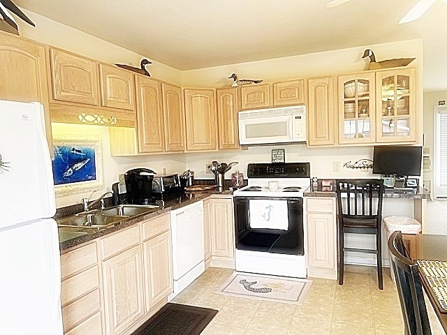 kitchen featuring white appliances, glass insert cabinets, a sink, and light brown cabinetry