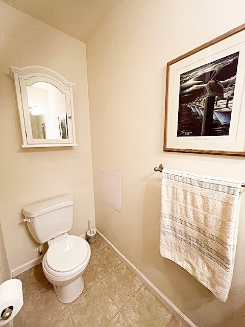 half bath featuring baseboards, toilet, and tile patterned floors