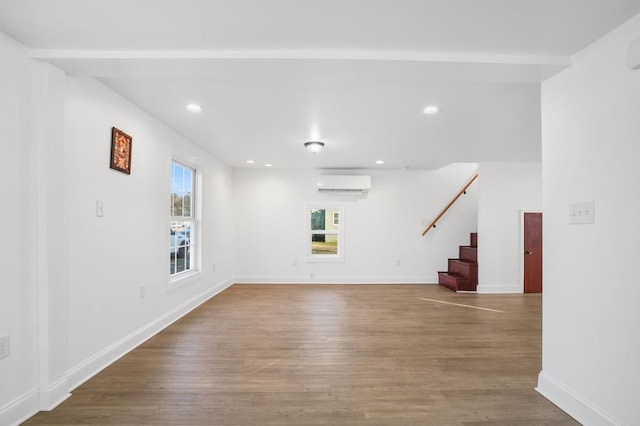 unfurnished room featuring beamed ceiling, a wall mounted air conditioner, and wood-type flooring