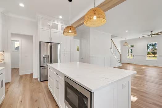 kitchen with stainless steel fridge, built in microwave, decorative light fixtures, a kitchen island, and white cabinetry