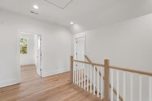 corridor with light wood-type flooring and vaulted ceiling