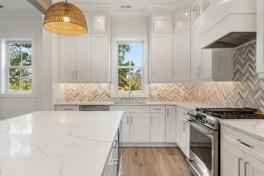 kitchen featuring backsplash, custom range hood, decorative light fixtures, white cabinets, and stainless steel stove