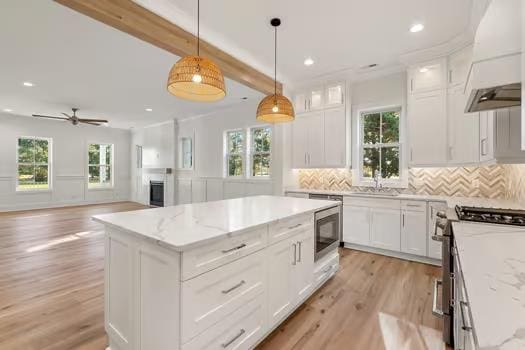 kitchen featuring a center island, hanging light fixtures, light stone counters, white cabinetry, and stainless steel appliances