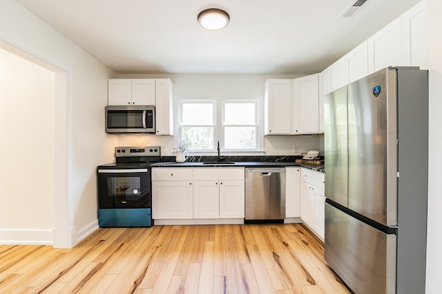 24455 Guilford Rd, Bloxom, VA 23308 - kitchen with stainless steel appliances, a sink, light wood-style flooring, dark countertops, and white cabinetry