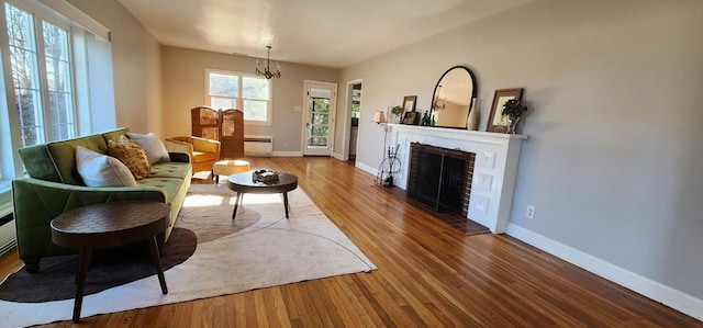 living area with a chandelier, a brick fireplace, wood finished floors, and baseboards