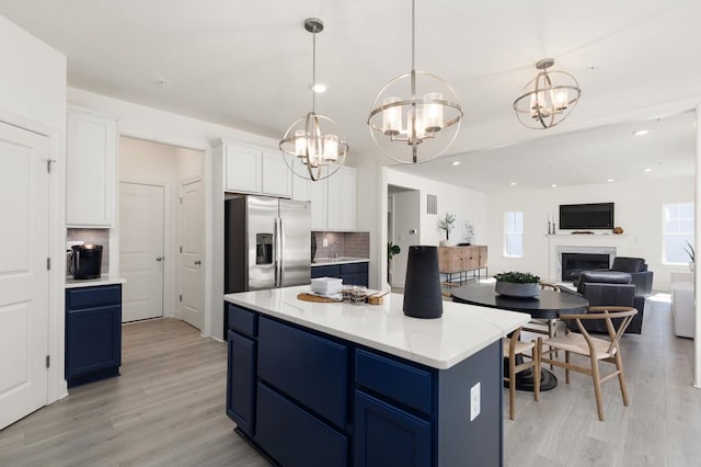 kitchen featuring white cabinets, stainless steel refrigerator with ice dispenser, decorative backsplash, and blue cabinetry