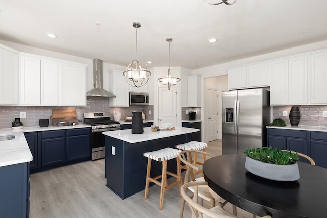 kitchen featuring wall chimney exhaust hood, stainless steel appliances, blue cabinets, pendant lighting, and a kitchen island