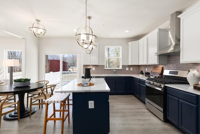 kitchen featuring an inviting chandelier, stainless steel range with gas cooktop, blue cabinets, wall chimney range hood, and decorative light fixtures