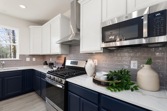 kitchen with appliances with stainless steel finishes, wall chimney exhaust hood, sink, blue cabinetry, and white cabinets