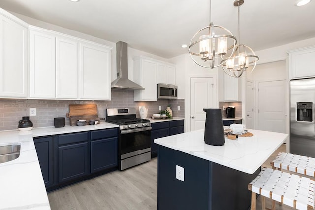 kitchen with white cabinetry, wall chimney exhaust hood, stainless steel appliances, pendant lighting, and a kitchen island