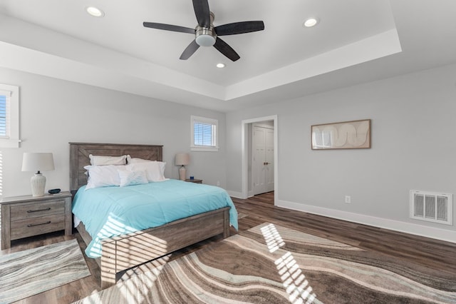 bedroom with ceiling fan, dark wood-type flooring, and a tray ceiling