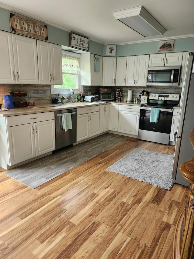 kitchen with decorative backsplash, white cabinets, light hardwood / wood-style floors, and appliances with stainless steel finishes