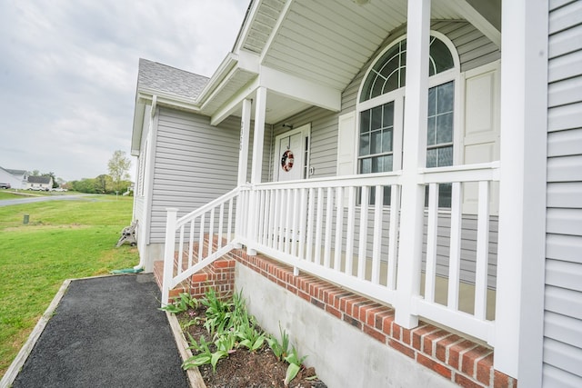doorway to property featuring a porch, a yard, and roof with shingles