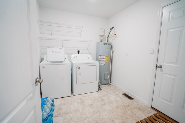 washroom with visible vents, baseboards, washer and dryer, electric water heater, and laundry area