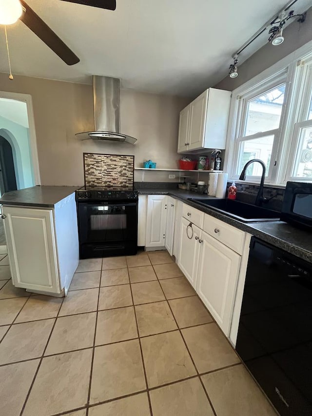 kitchen with sink, white cabinets, black appliances, and wall chimney range hood