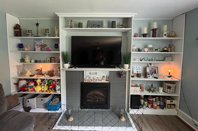 living room featuring wood-type flooring, crown molding, and a tiled fireplace