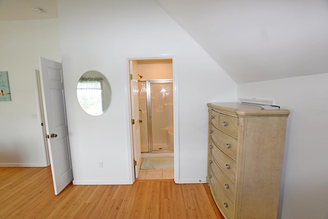 unfurnished bedroom with vaulted ceiling, ensuite bathroom, and light hardwood / wood-style flooring