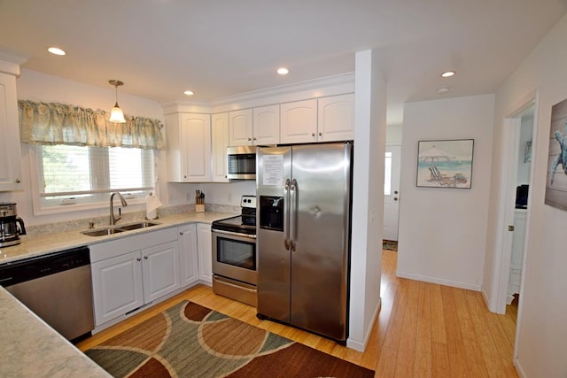 kitchen with sink, hanging light fixtures, stainless steel appliances, light hardwood / wood-style floors, and white cabinets