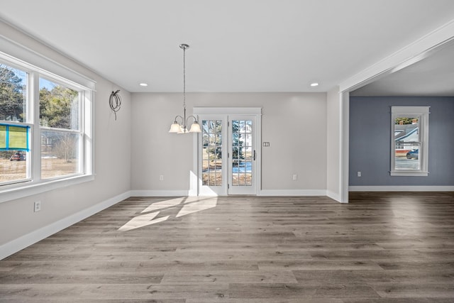 unfurnished dining area featuring an inviting chandelier, wood-type flooring, and plenty of natural light