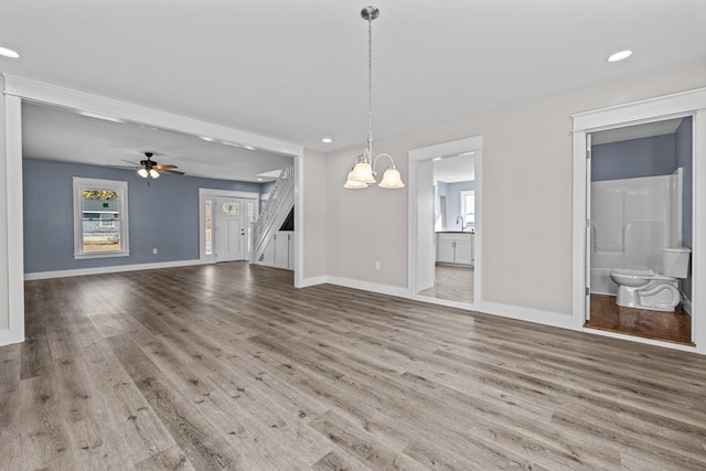 unfurnished living room featuring ceiling fan with notable chandelier and wood-type flooring