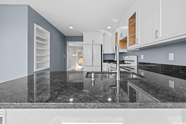 kitchen featuring sink, white appliances, white cabinetry, dark stone countertops, and kitchen peninsula