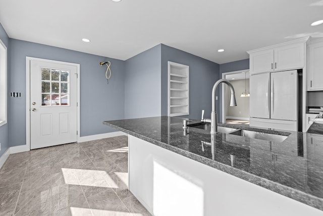 kitchen with white fridge, sink, dark stone countertops, and white cabinets