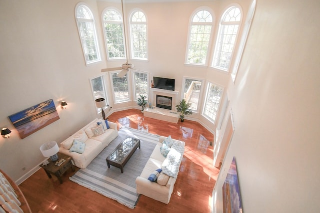 living room featuring ceiling fan, a towering ceiling, a high end fireplace, and wood-type flooring