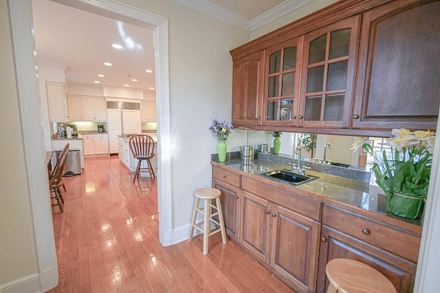 bar featuring dark stone countertops, sink, light hardwood / wood-style flooring, and ornamental molding