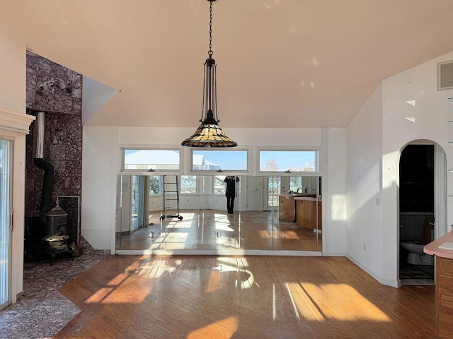 unfurnished living room featuring a high ceiling, hardwood / wood-style floors, a healthy amount of sunlight, and a wood stove