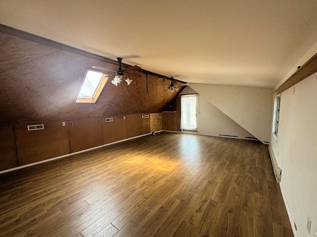 additional living space with a baseboard heating unit, dark hardwood / wood-style floors, vaulted ceiling with skylight, and ceiling fan