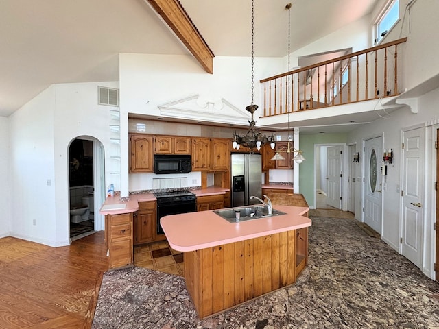 kitchen featuring range, high vaulted ceiling, stainless steel refrigerator with ice dispenser, a center island with sink, and beamed ceiling