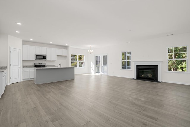 unfurnished living room with sink, a chandelier, and light wood-type flooring