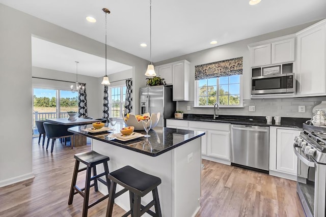 kitchen with decorative light fixtures, a kitchen island, white cabinetry, and appliances with stainless steel finishes