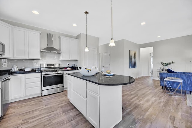 kitchen featuring wall chimney exhaust hood, stainless steel gas range oven, a kitchen island, and white cabinetry