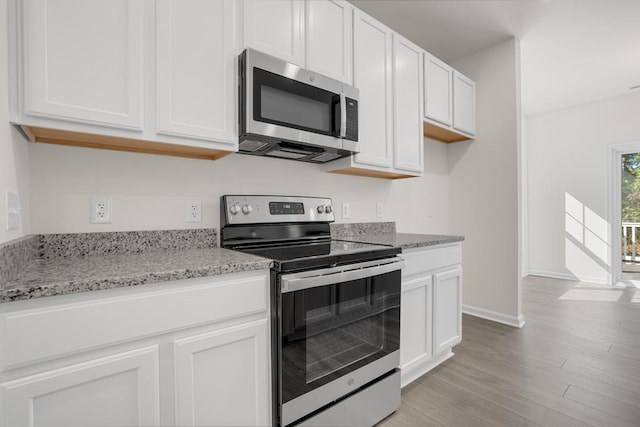 kitchen featuring light stone countertops, stainless steel appliances, white cabinetry, and light hardwood / wood-style flooring