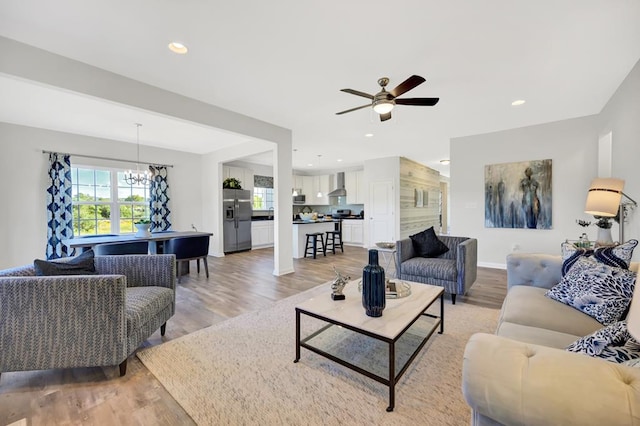 living room with ceiling fan with notable chandelier and light hardwood / wood-style flooring