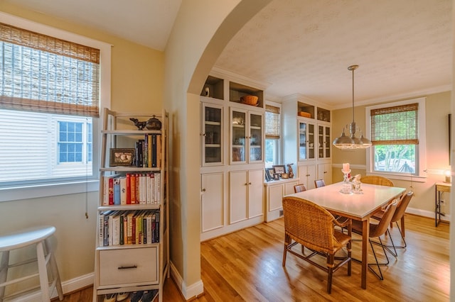 dining area featuring light wood-type flooring, arched walkways, and baseboards